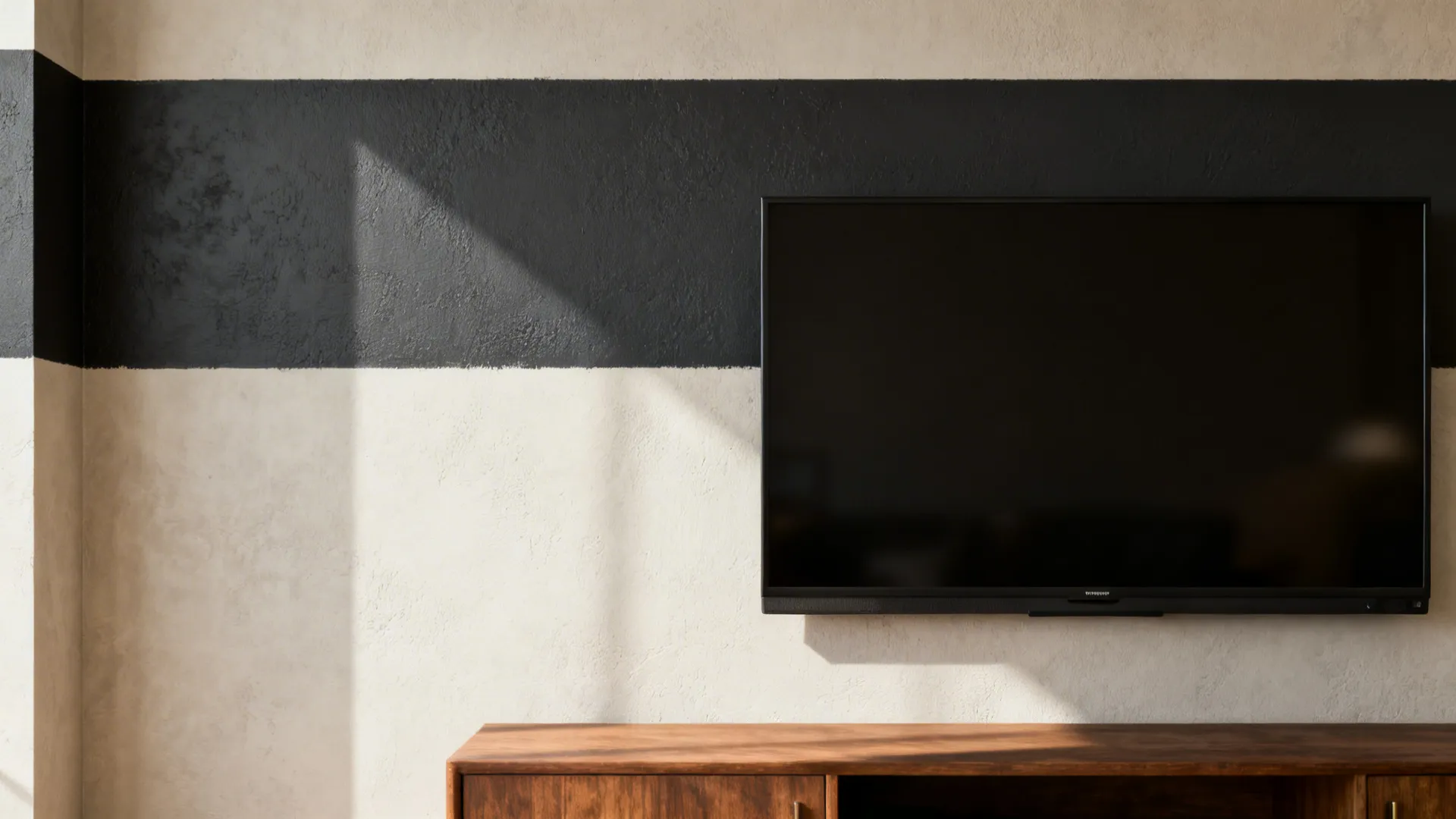 Modern black flat-screen television on beige wall with dark horizontal stripe and wooden storage cabinet