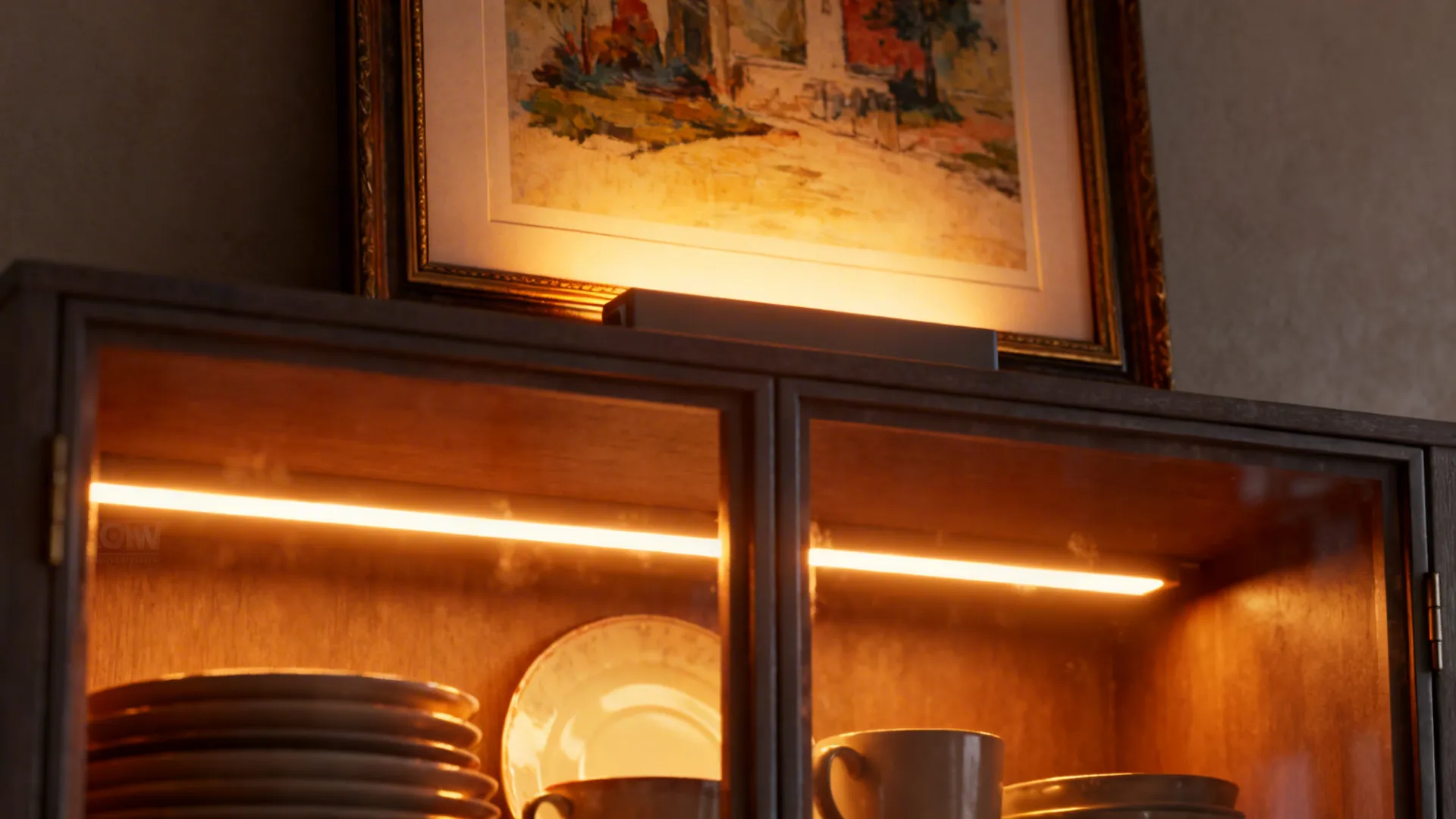 Glass-front cabinet lit by warm LED strip lights with dishes glowing and picture light above art