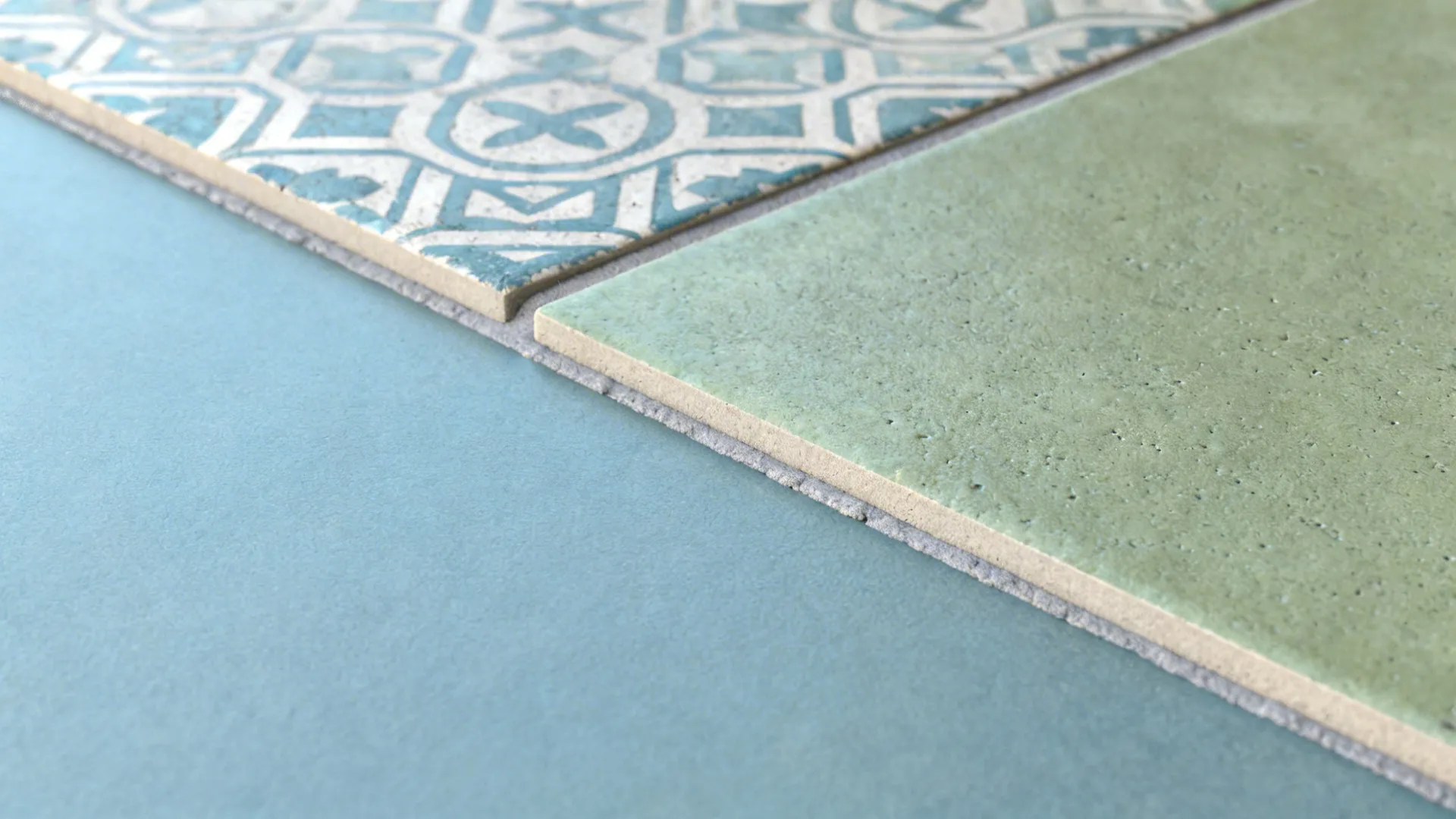 Close up of patterned blue tile and green tile meeting on light blue floor surface