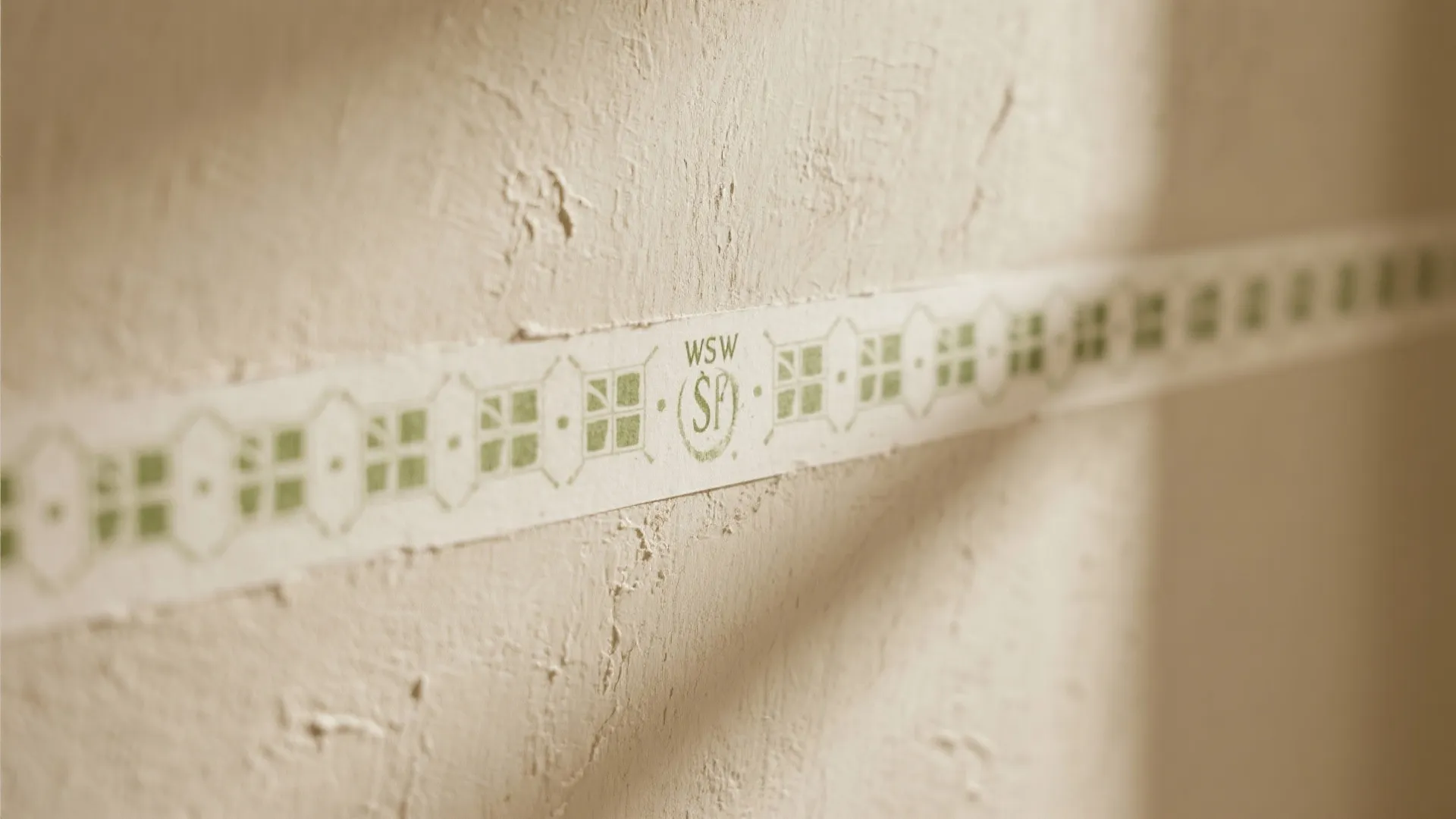 Close up of textured beige wall with decorative patterned paper border showing green window icons