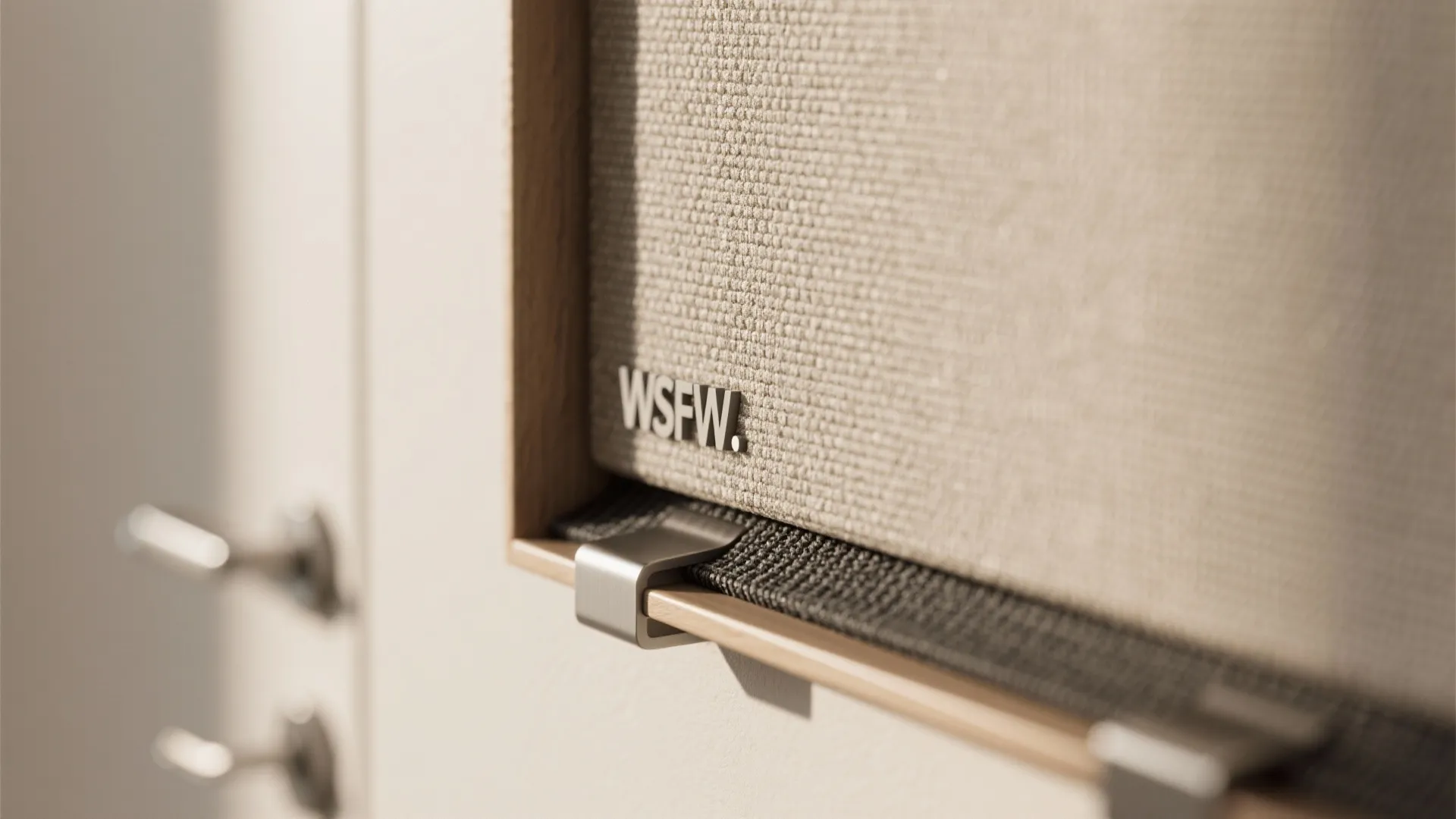 Beige fabric wall panel detail showing a small metal logo and a silver metal clip