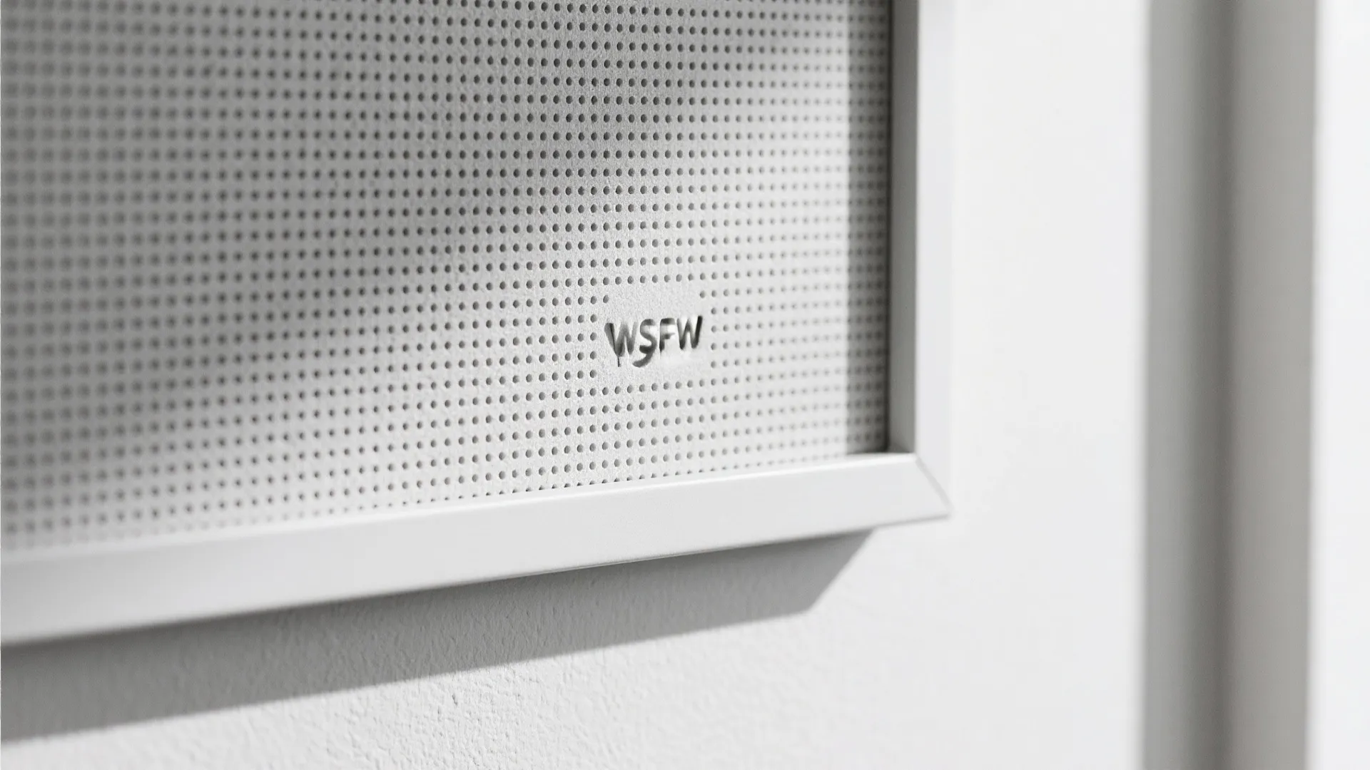 Close up view of a white wall panel with small holes and a simple metal frame