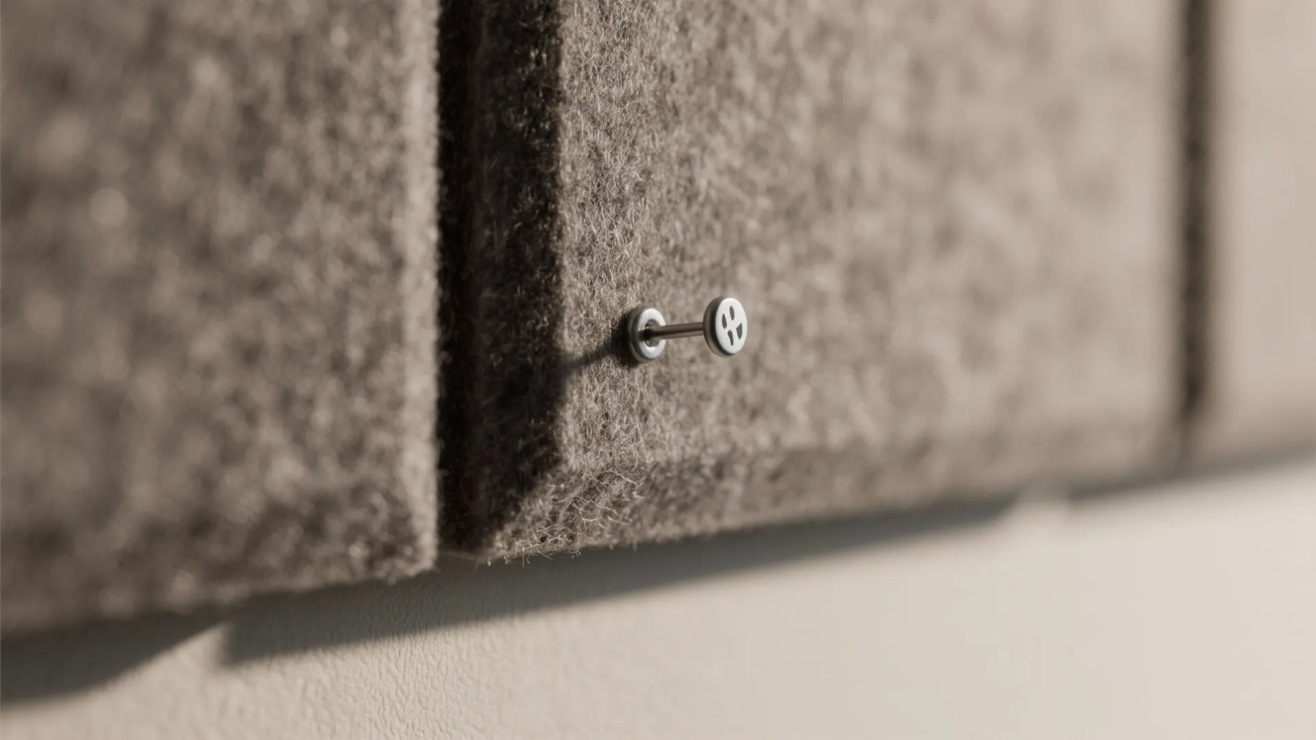 Close up of grey wall panel texture with a small metal pin and soft shadows