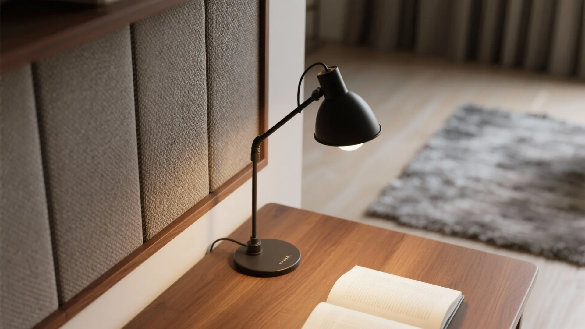 Black desk light on wooden table with open book next to grey padded wall panel