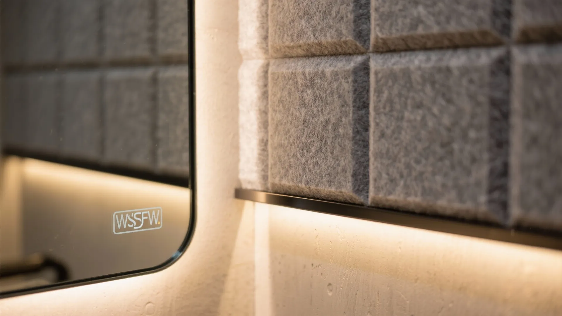 Modern bathroom mirror with built in light placed next to grey textured square wall panels
