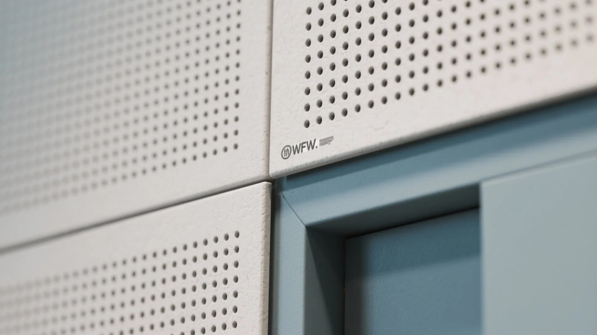 Close up view of white wall panel with small holes and blue trim in modern interior
