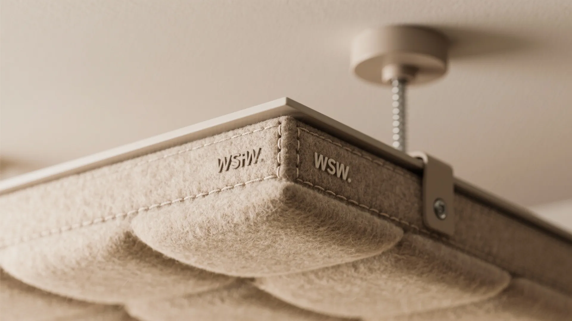 Close up of a beige fabric ceiling panel showing visible white stitching and metal fixture