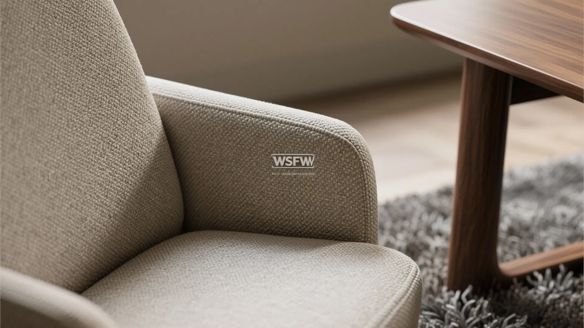 Close up of a beige fabric chair armrest next to a wood table and grey rug