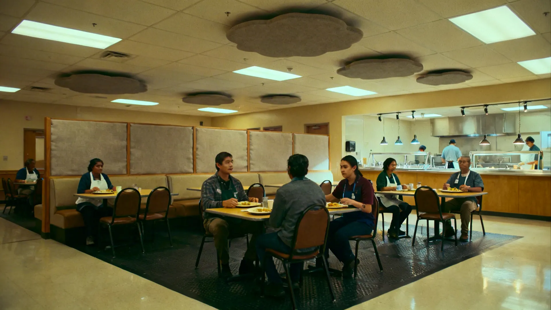 People sitting at tables in a cafeteria with cloud shaped ceiling panels and recessed lights