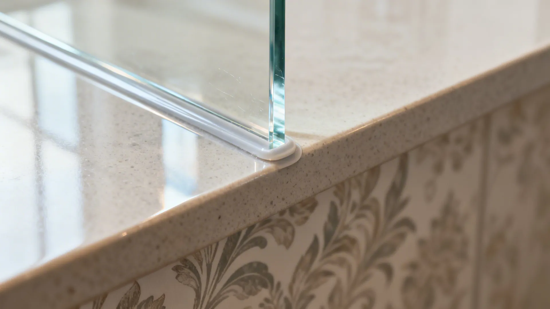 Macro of clear acrylic splashback edge with neat silicone seal showing wallpaper beneath.