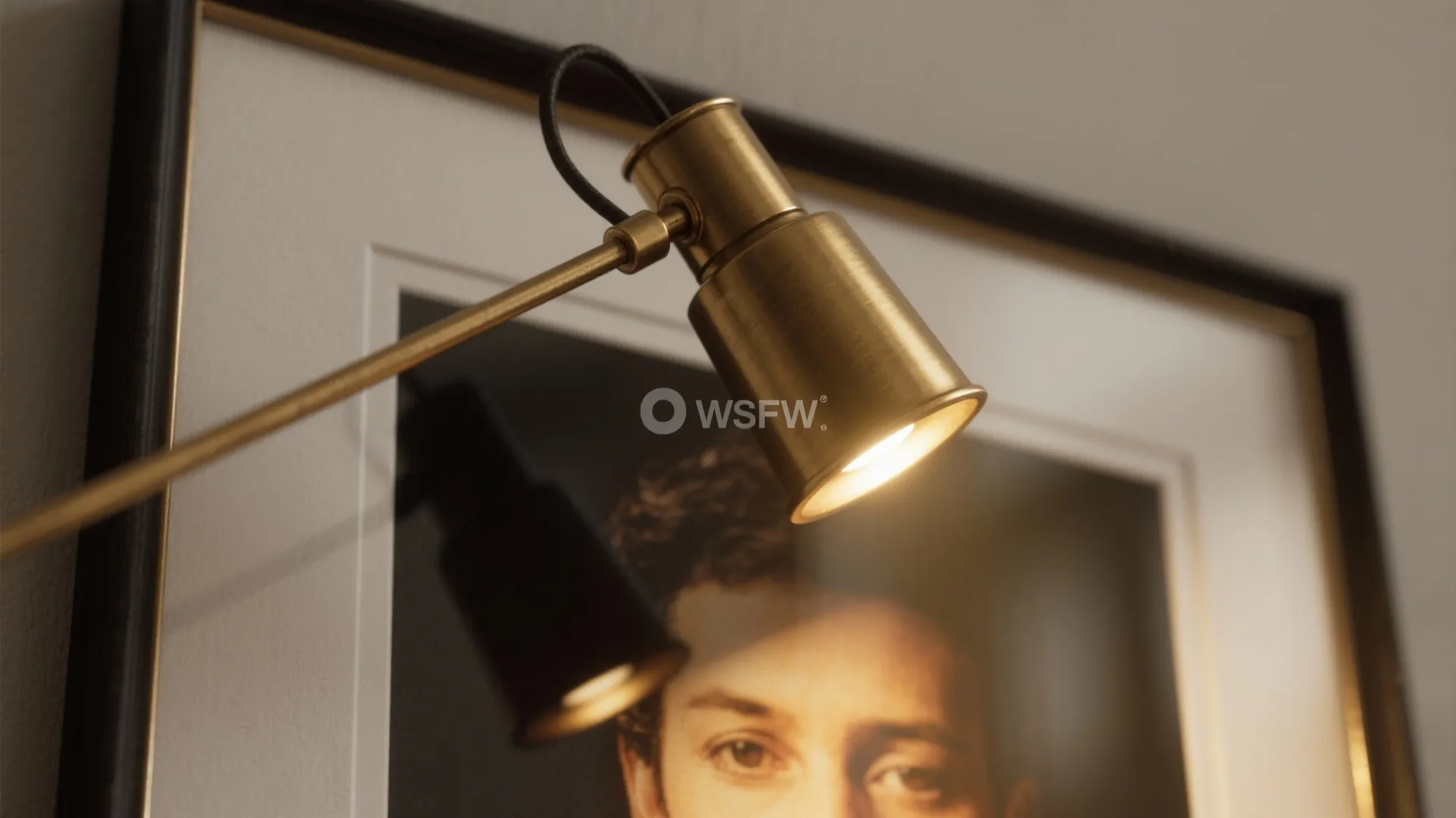 Brass wall light fixture shining warm light onto a framed portrait picture hanging on the wall