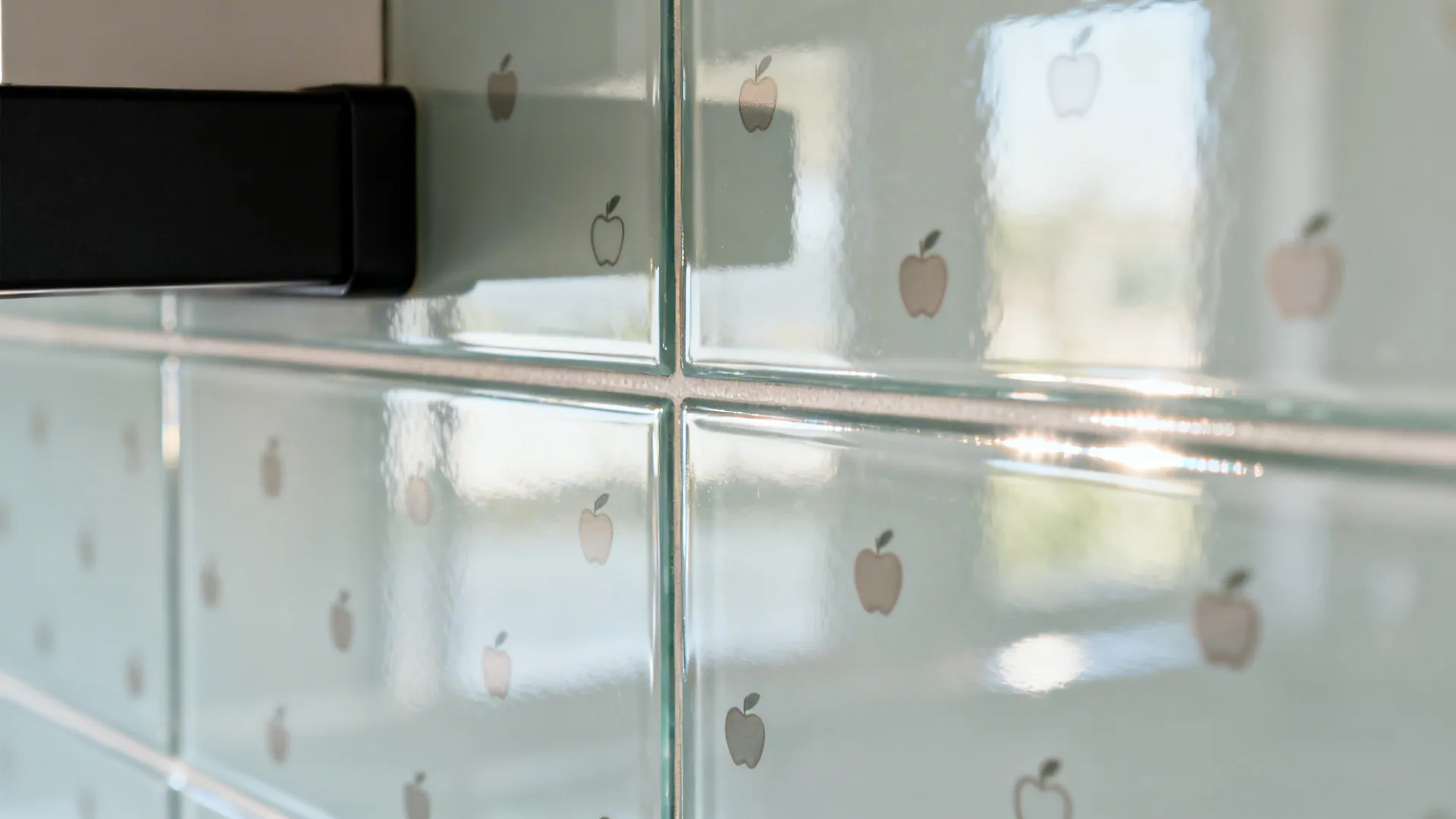 Macro of glossy glass-look backsplash with tiny apple decals creating subtle reflections.