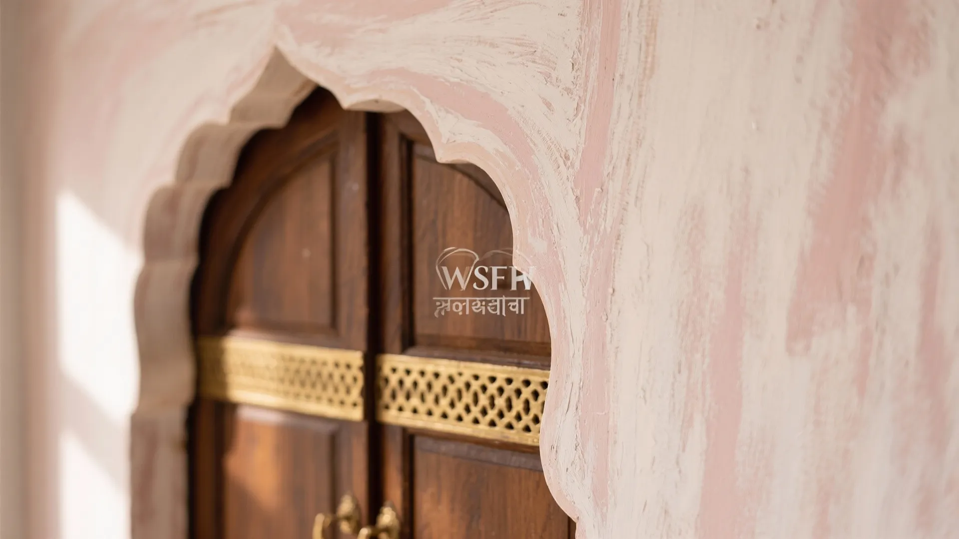 Arched dark wood door with gold metal details set in a pink and white wall