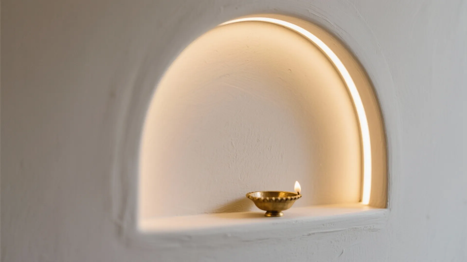 White wall niche with arched light strip and small gold lamp on a clean shelf