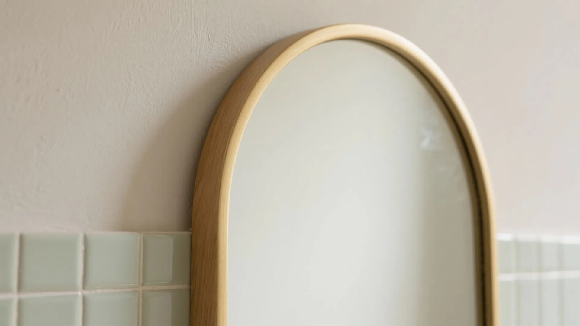 Macro of slim brass arched mirror frame with a clean reveal against limewash and tile.