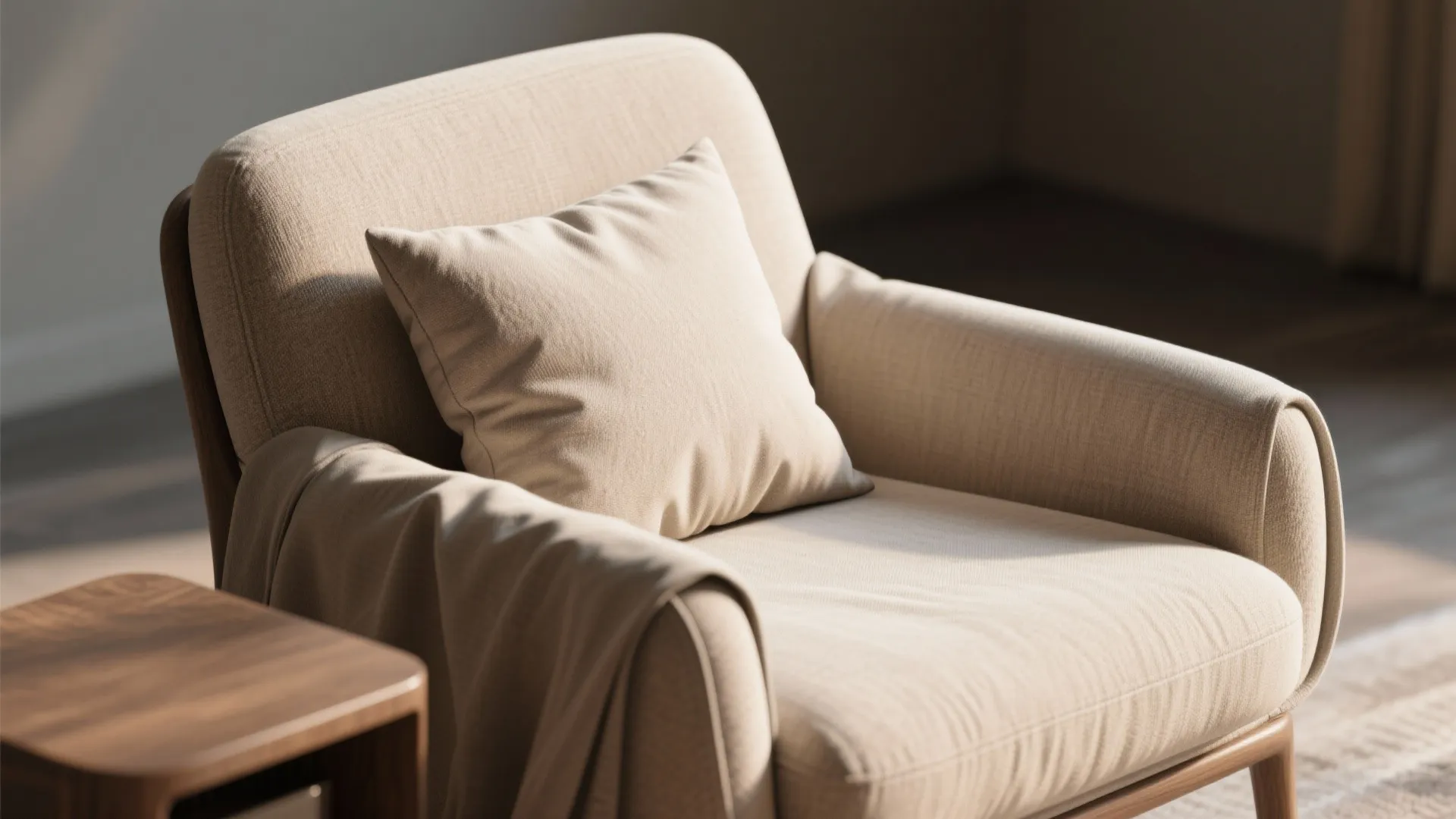 Comfortable beige fabric chair with a soft pillow and brown blanket next to wooden table