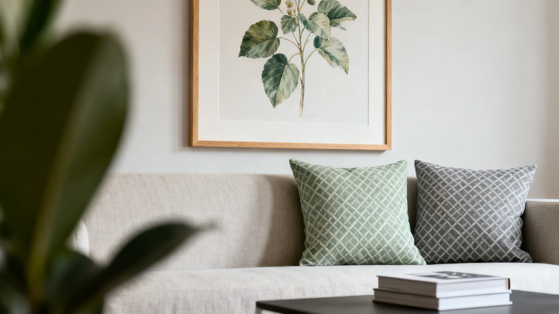 Framed botanical print above sofa with small-scale geometric cushions in sage and grey