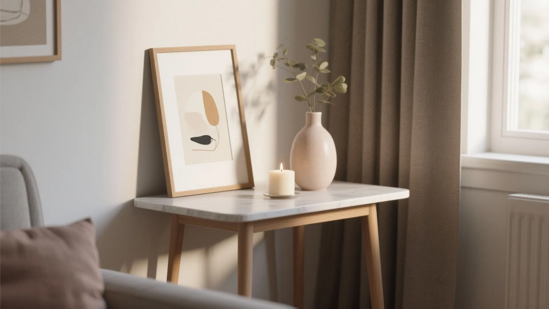 Marble side table featuring a framed art print, lit candle, and green leaves in vase