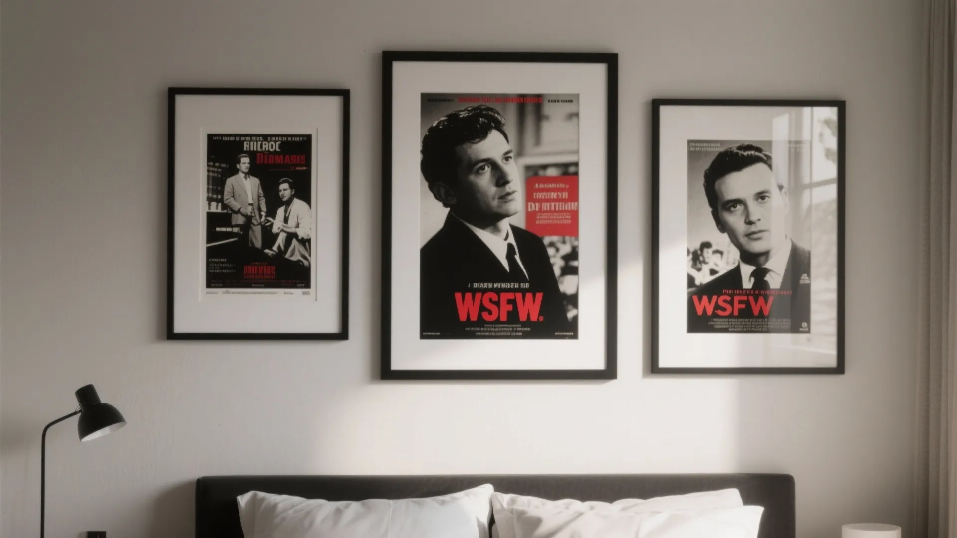 Three framed movie posters on white wall above bed with black lamp and white pillows