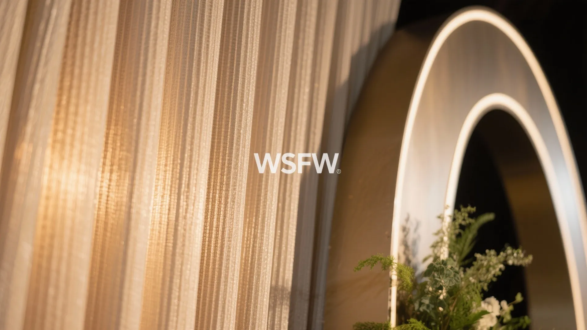 Close up of beige curtain fabric with round light fixture and green plants in warm lighting