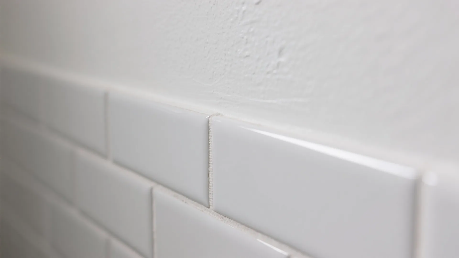 Close up of white rectangular wall tiles meeting a clean white painted wall surface detail