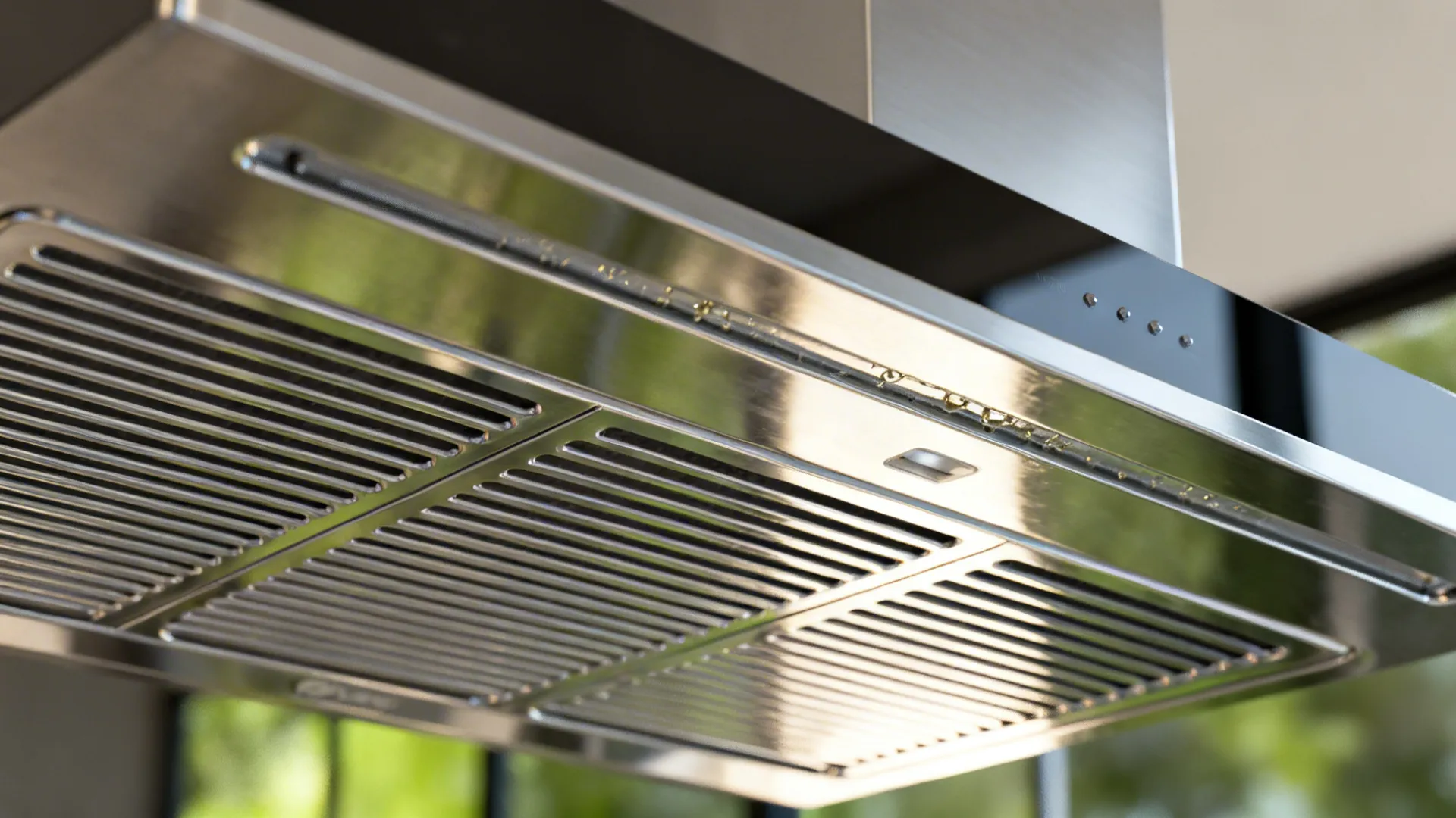 Macro view of stainless baffle filters and grease channel under a modern range hood.