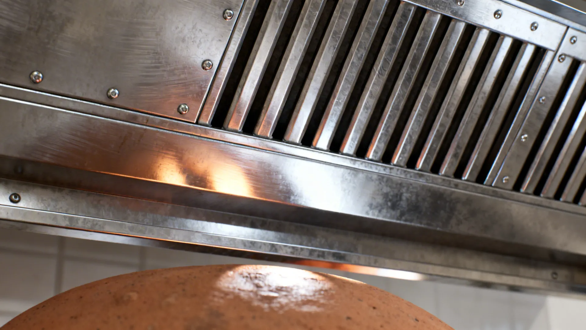 Macro of stainless baffle filters and hood side panel above a tandoor.