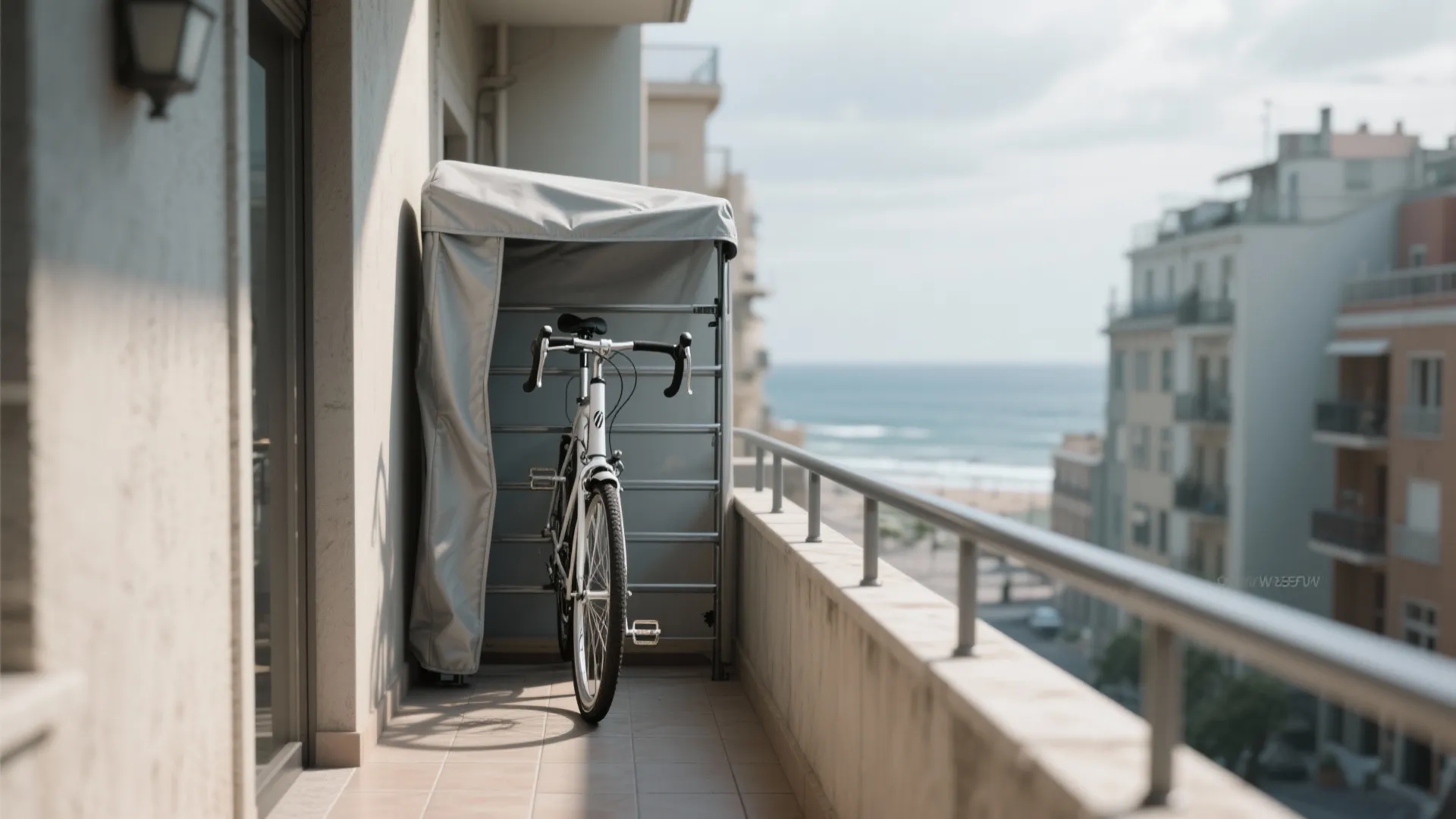 White bicycle parked on a balcony inside a grey storage cover with a sea view background