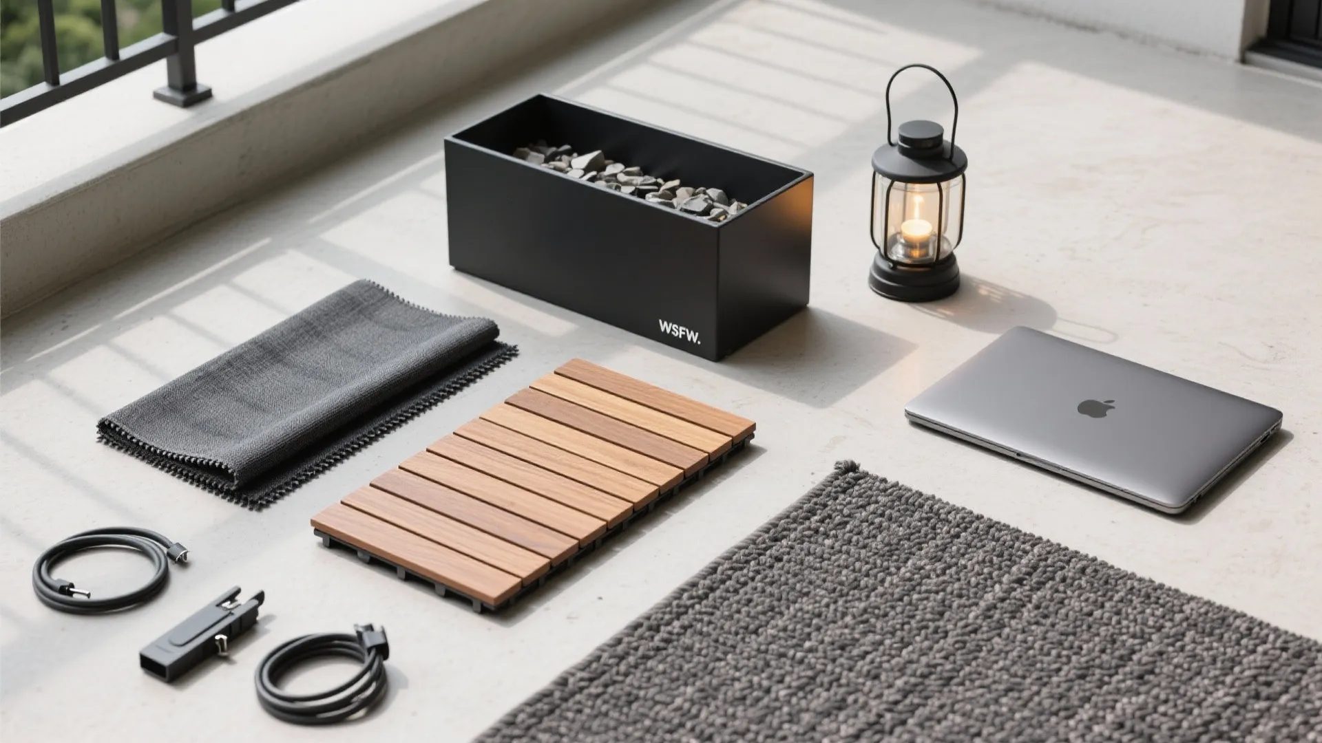 Flat lay of balcony materials including wood tiles grey rug laptop lantern and black metal box