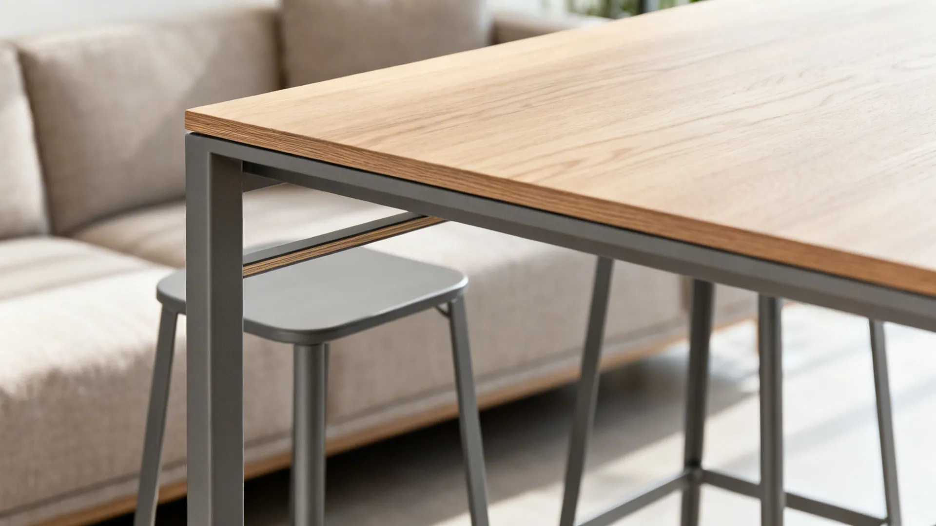 Modern wooden top table with grey metal legs next to grey stool and soft beige sofa