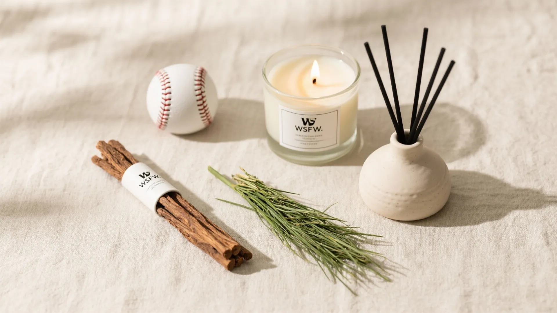 Scented candle with wood sticks and a small baseball on a beige textured cloth surface