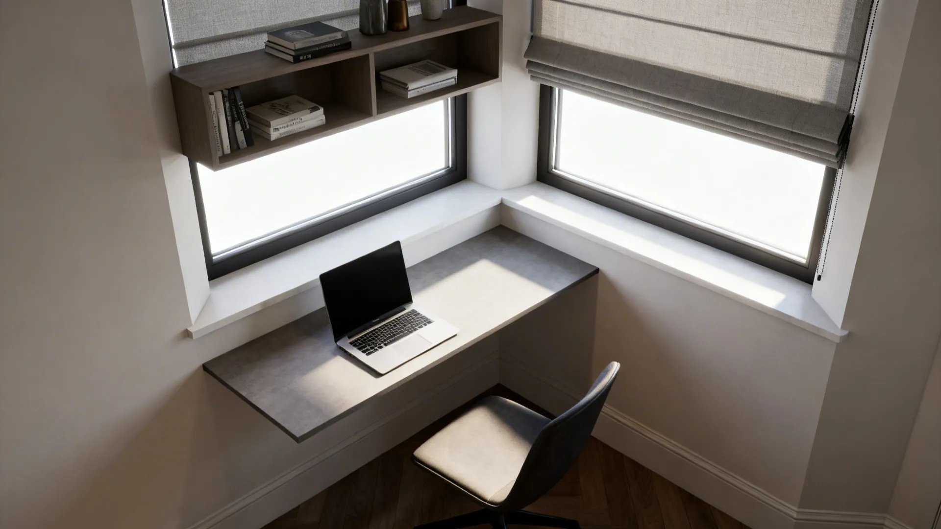 Small home office corner with gray desk, laptop, black chair, wall shelf, and window blinds