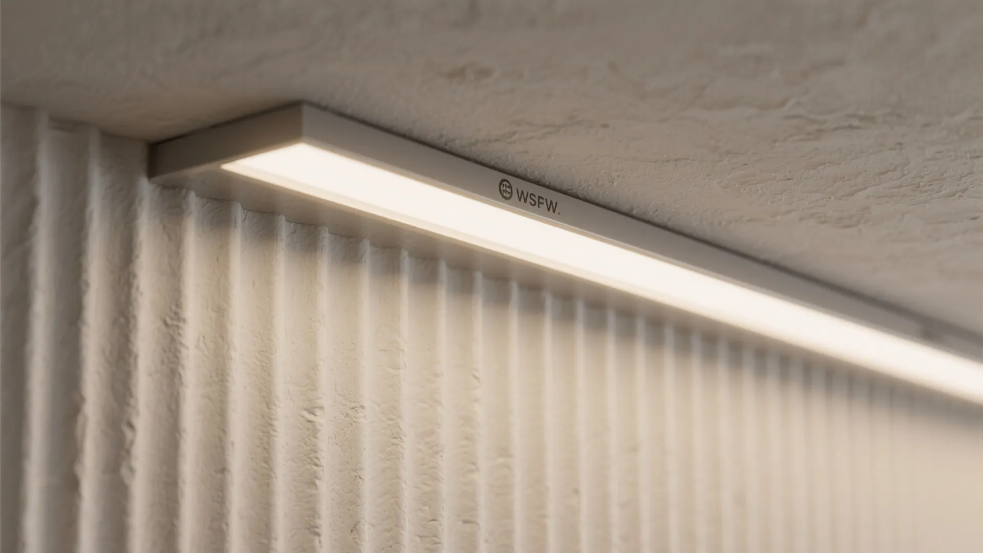 Close up of a linear light fixture installed on a textured white wall panel surface