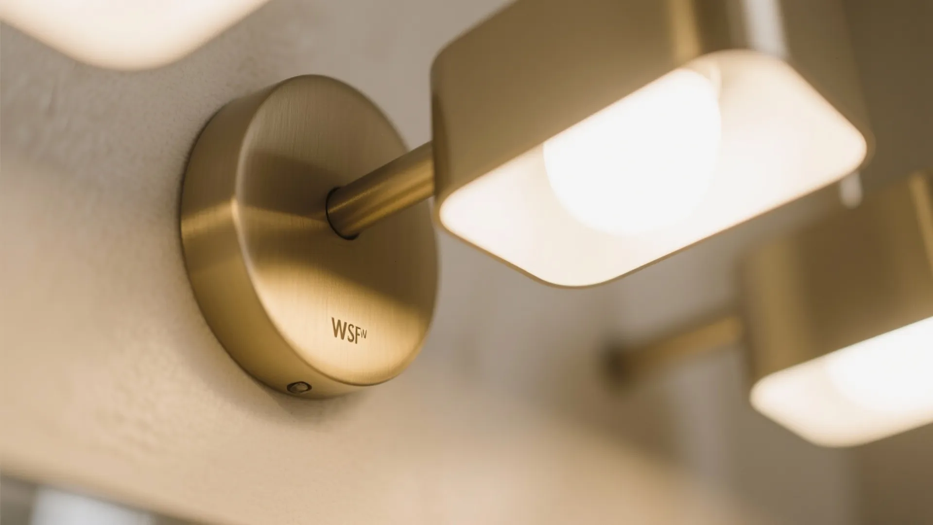 Close-up of gold wall lights with square glowing bulbs mounted on a neutral colored wall