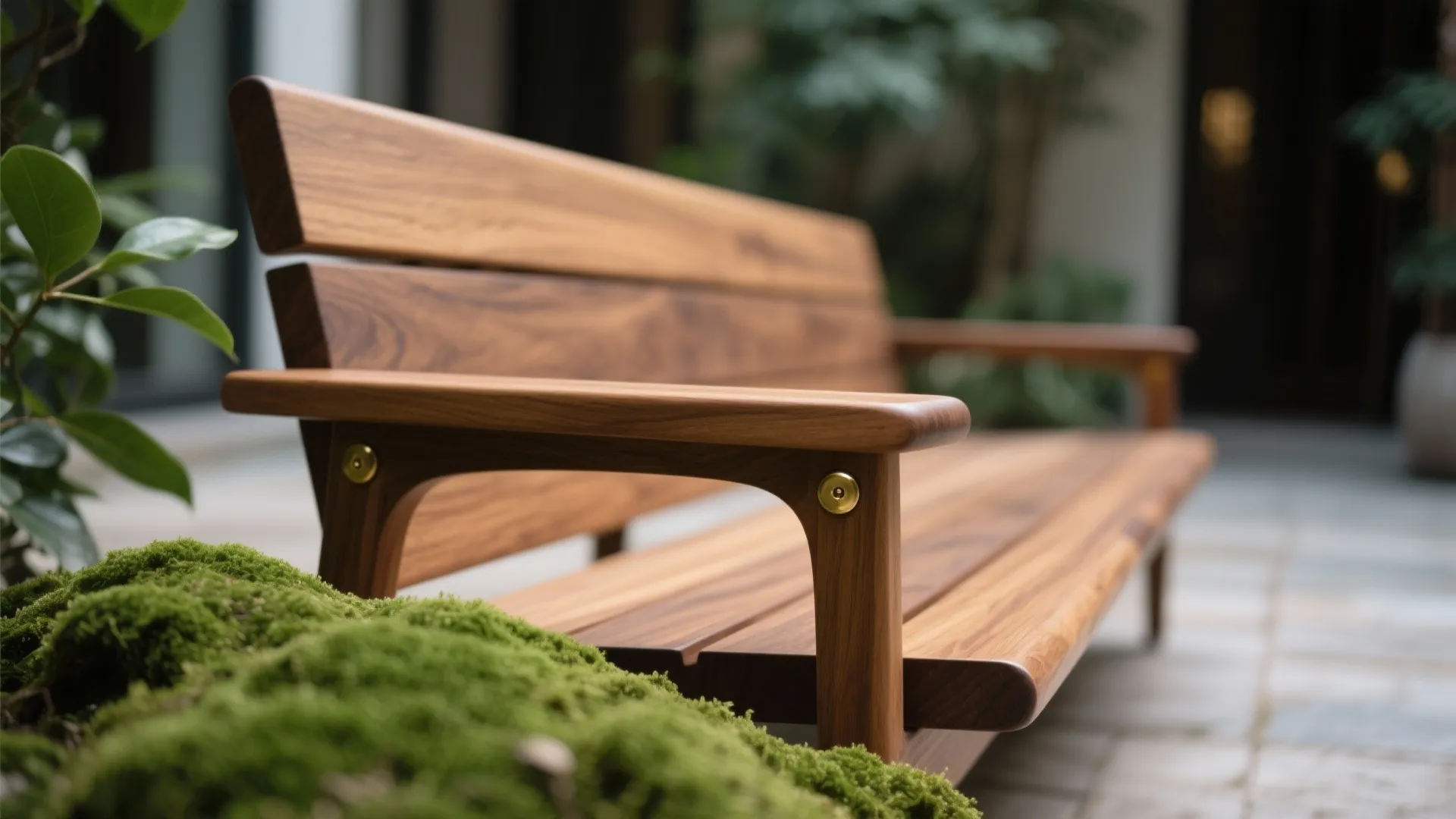 Wooden outdoor bench armrest featuring gold metal hardware details with green moss in the foreground