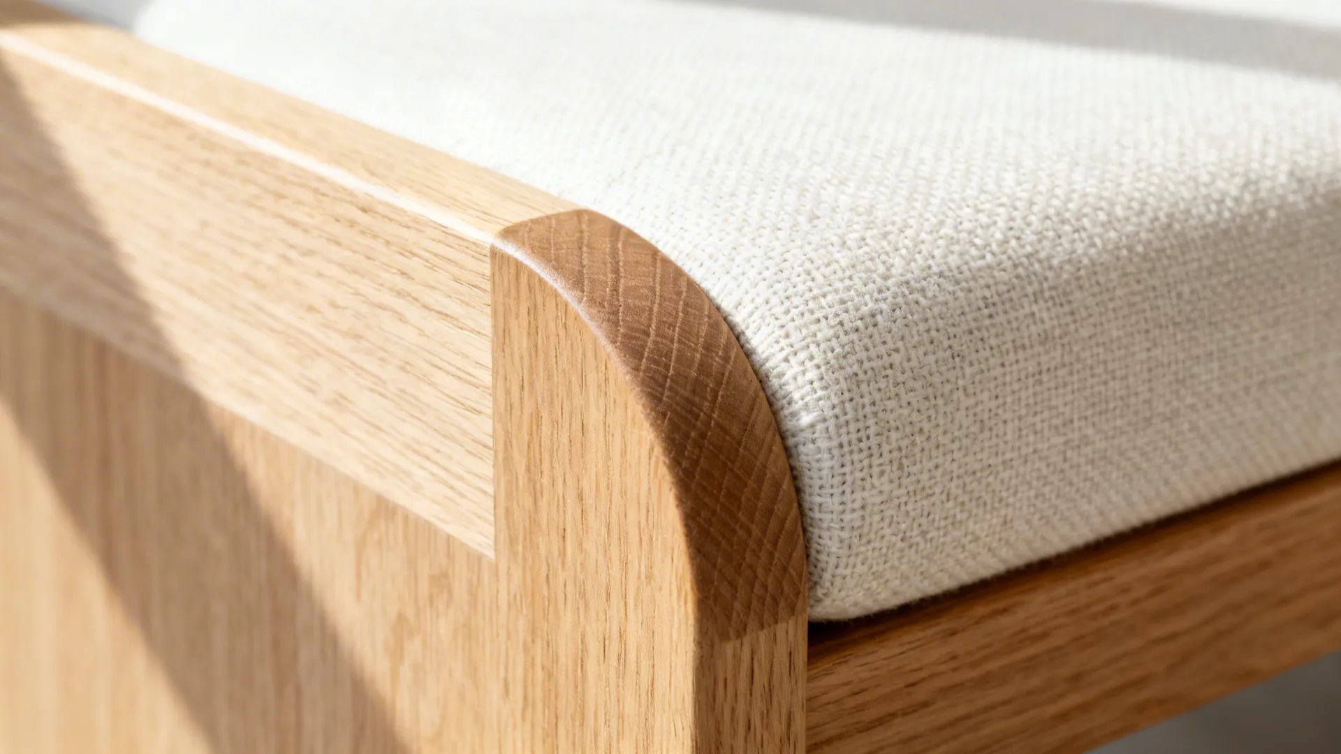 Close-up of a rounded ash bench edge with a linen cushion in soft light.