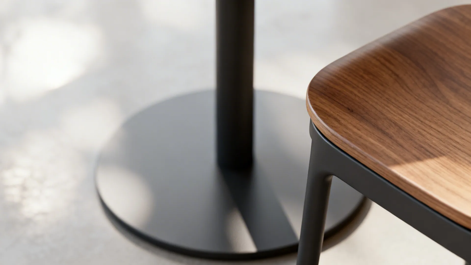 Detailed view of black round table base and wooden chair seat on a light floor