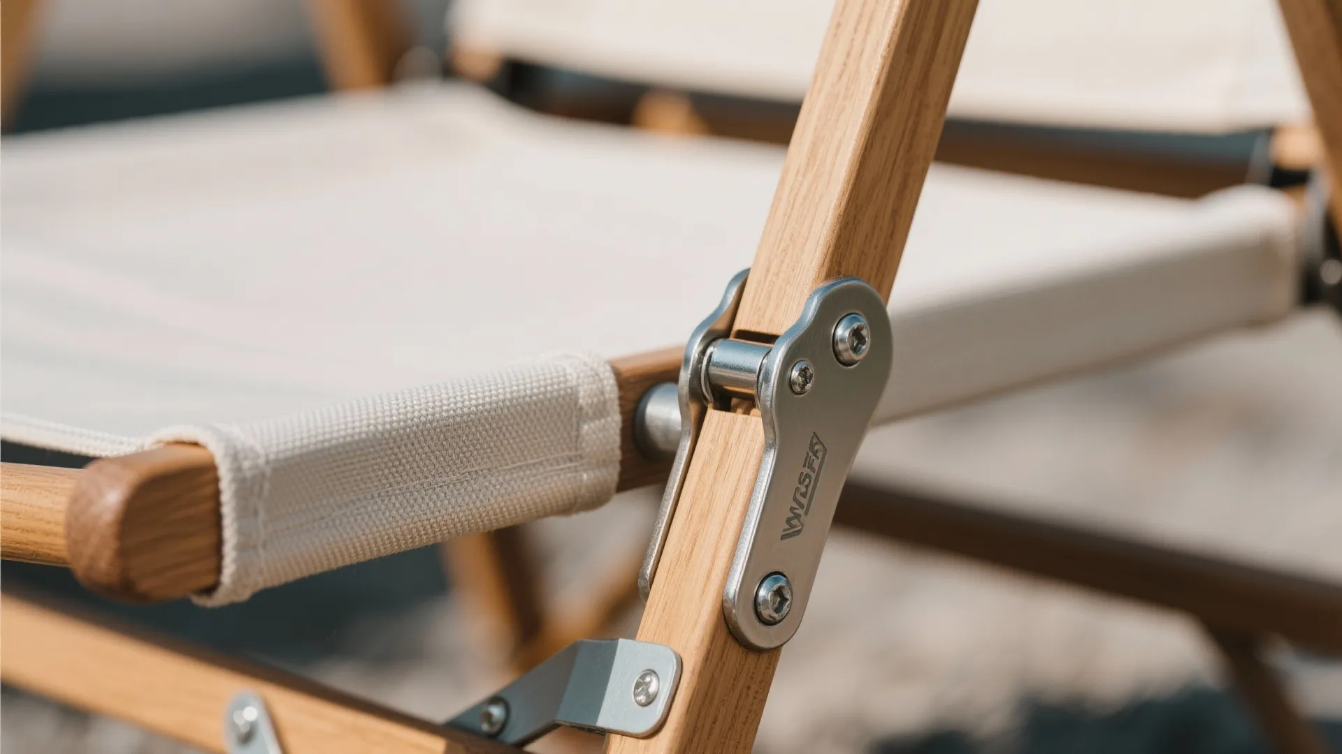 Detailed view of metal hinge hardware on a wooden folding chair with white fabric seat material