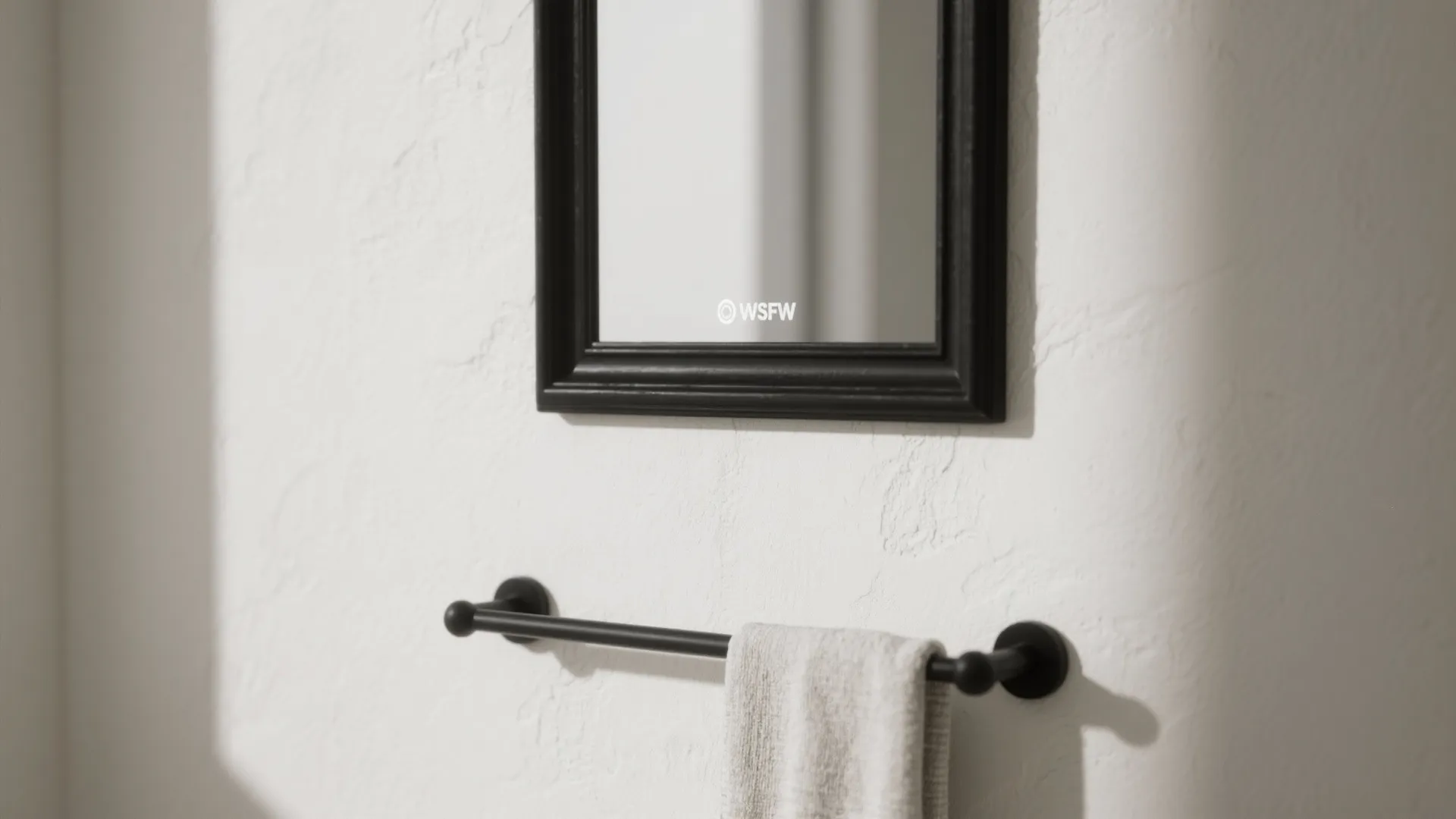 Matte black mirror frame and towel bar as a single accent on off-white walls.