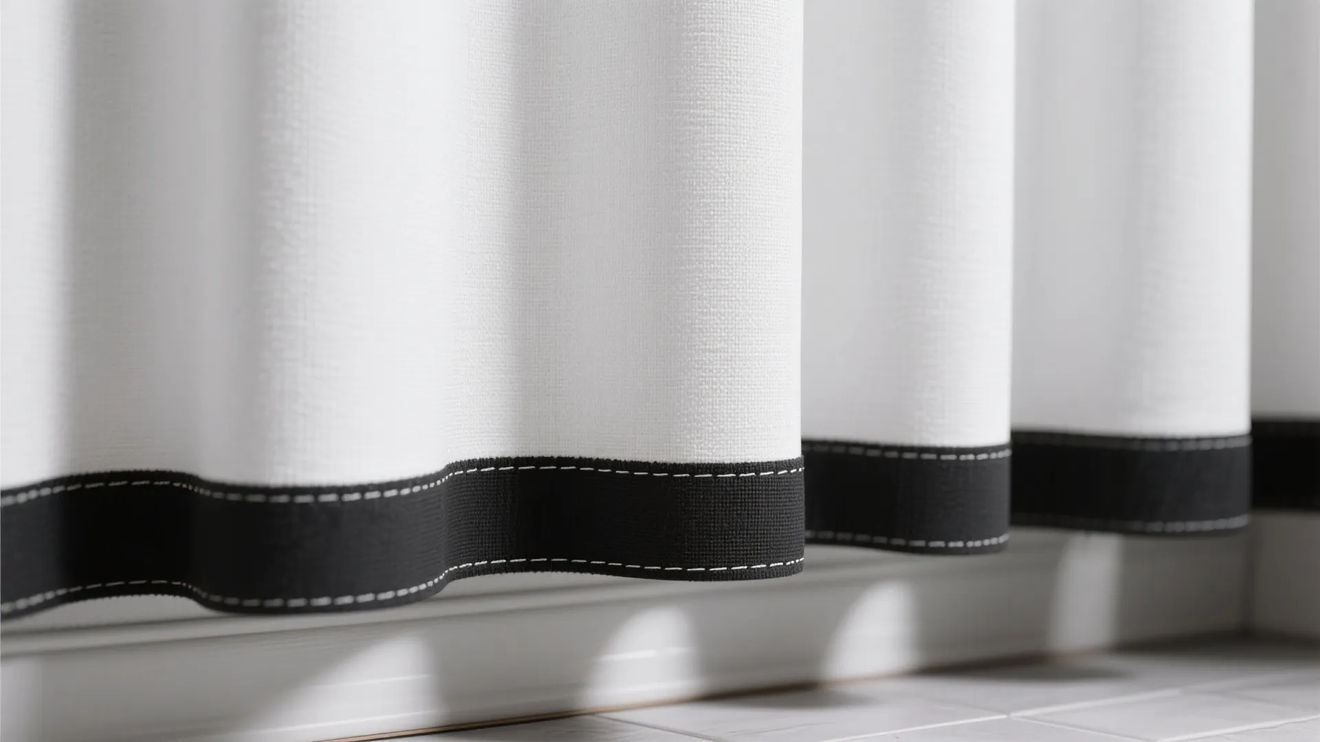 Close up view of white fabric curtain with a black border along the bottom edge