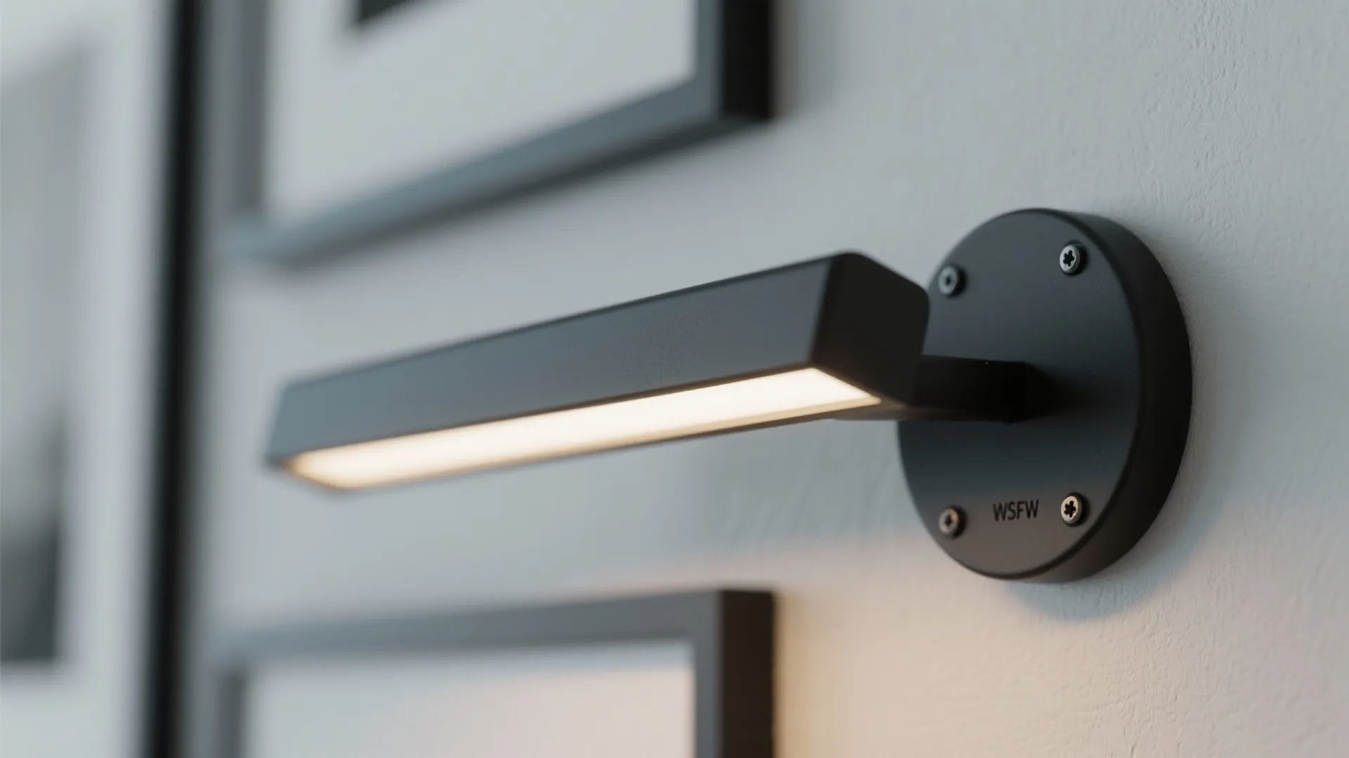 Modern black wall light mounted on a white wall illuminating picture frames in a room