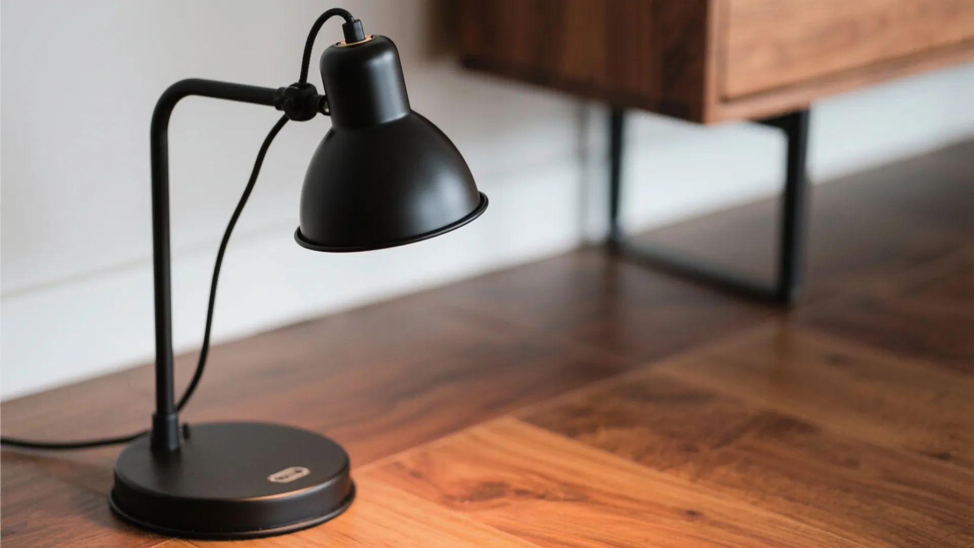 Black metal light fixture sitting on a wooden desk next to a modern wooden cabinet