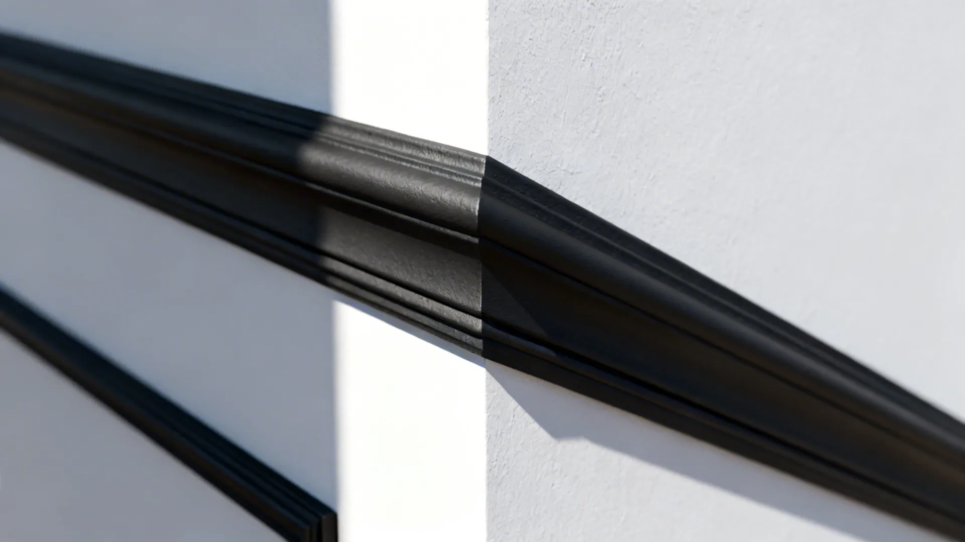 Close-up of clean geometric black moldings on a white wall showing sharp caulking and texture.