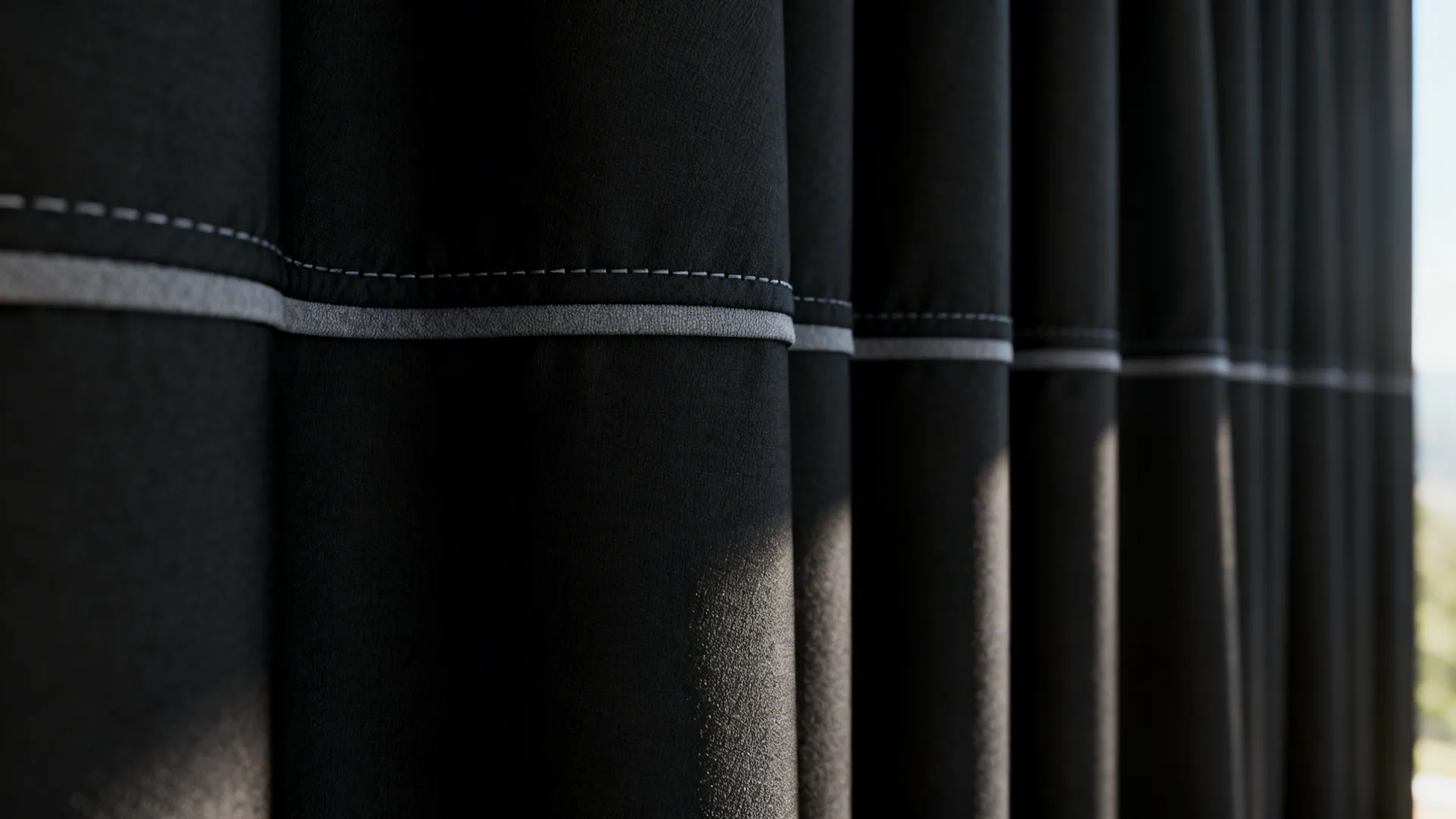 Close up of black fabric curtain with a thin horizontal grey stripe and white stitching
