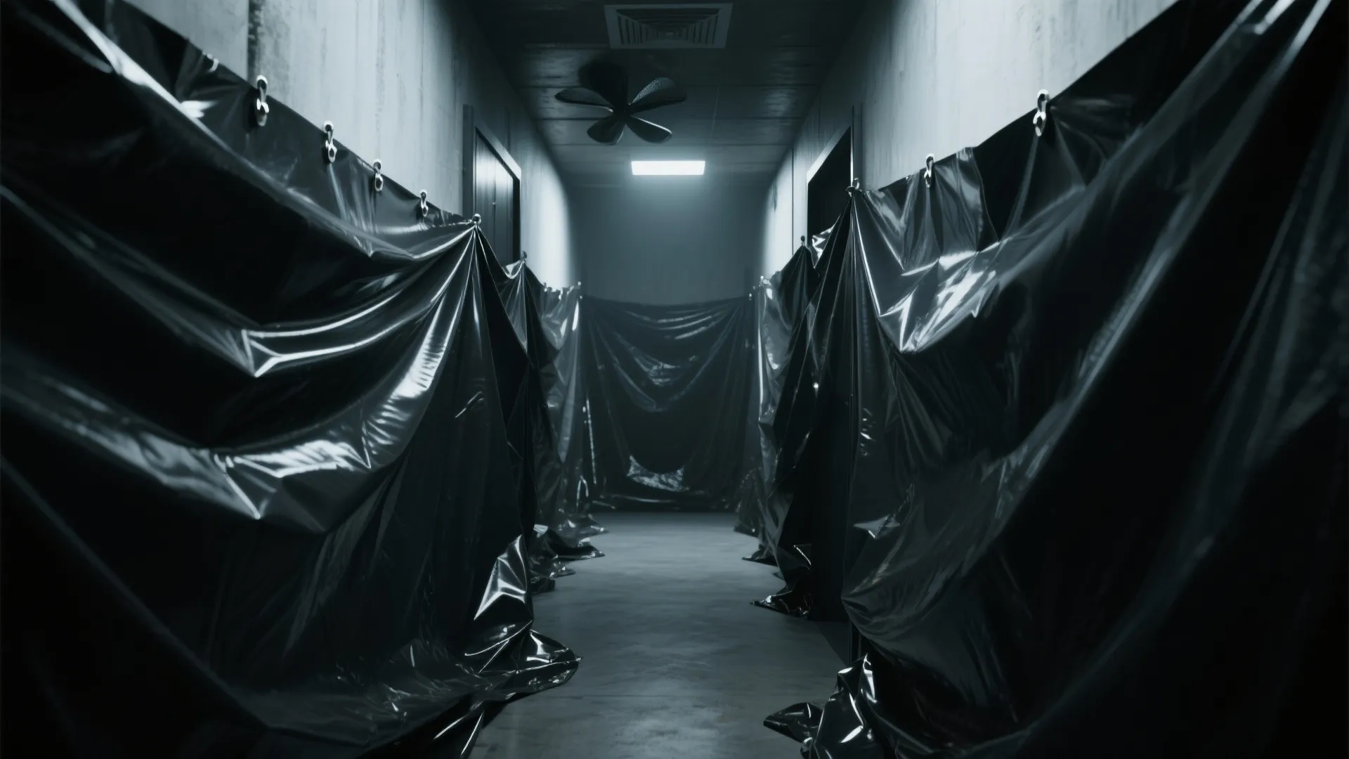 Dark hallway with walls covered in black plastic sheets ceiling fan and a single overhead light
