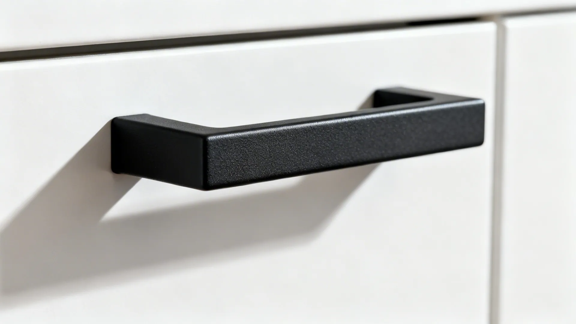 Macro of a matte-black bar pull on a smooth white cabinet door.