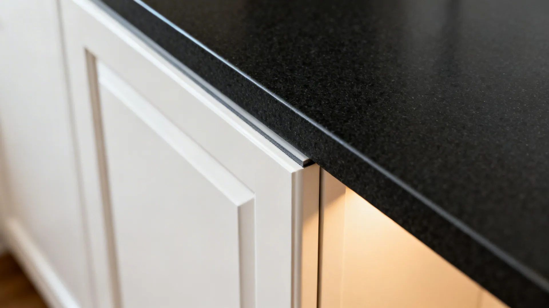 Macro view of matte black quartz edge next to a white cabinet door.
