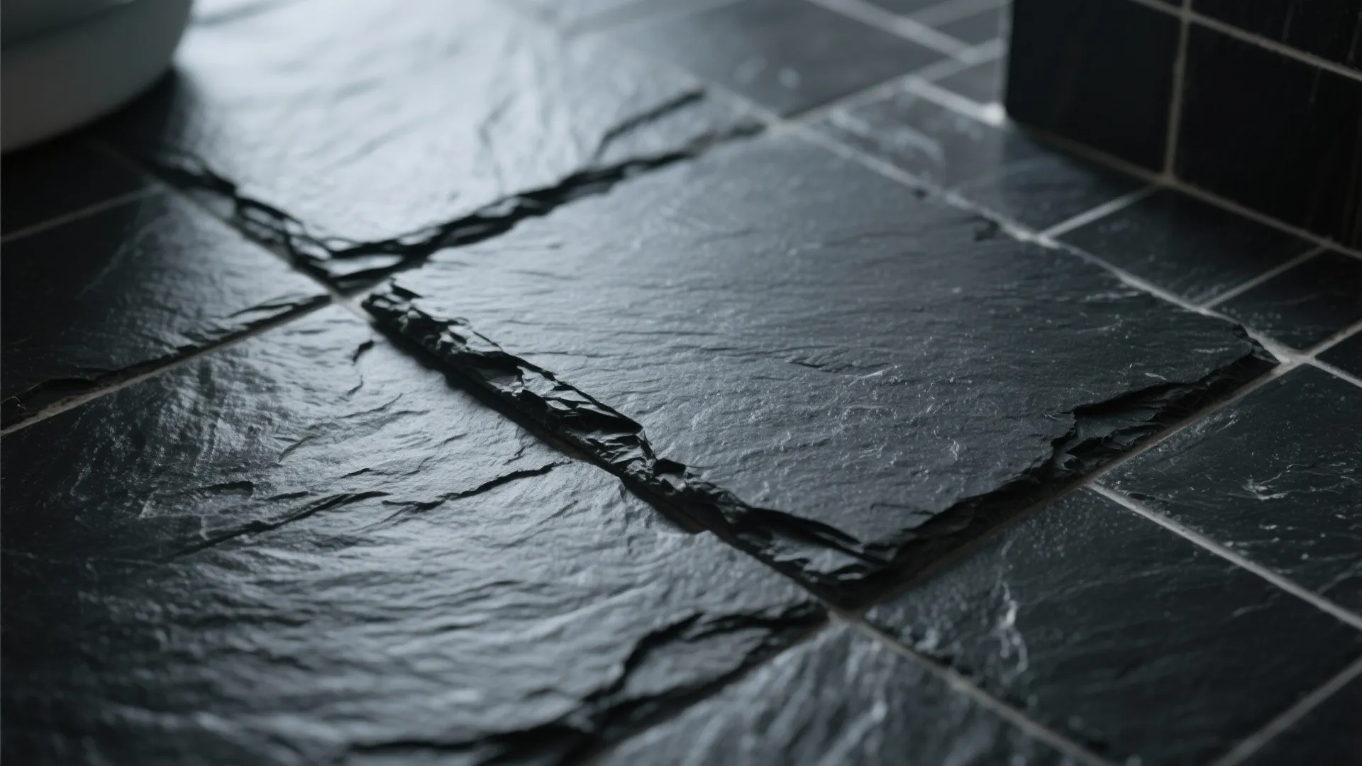 Close-up of textured black stone floor tiles with natural rough surface and white grout lines