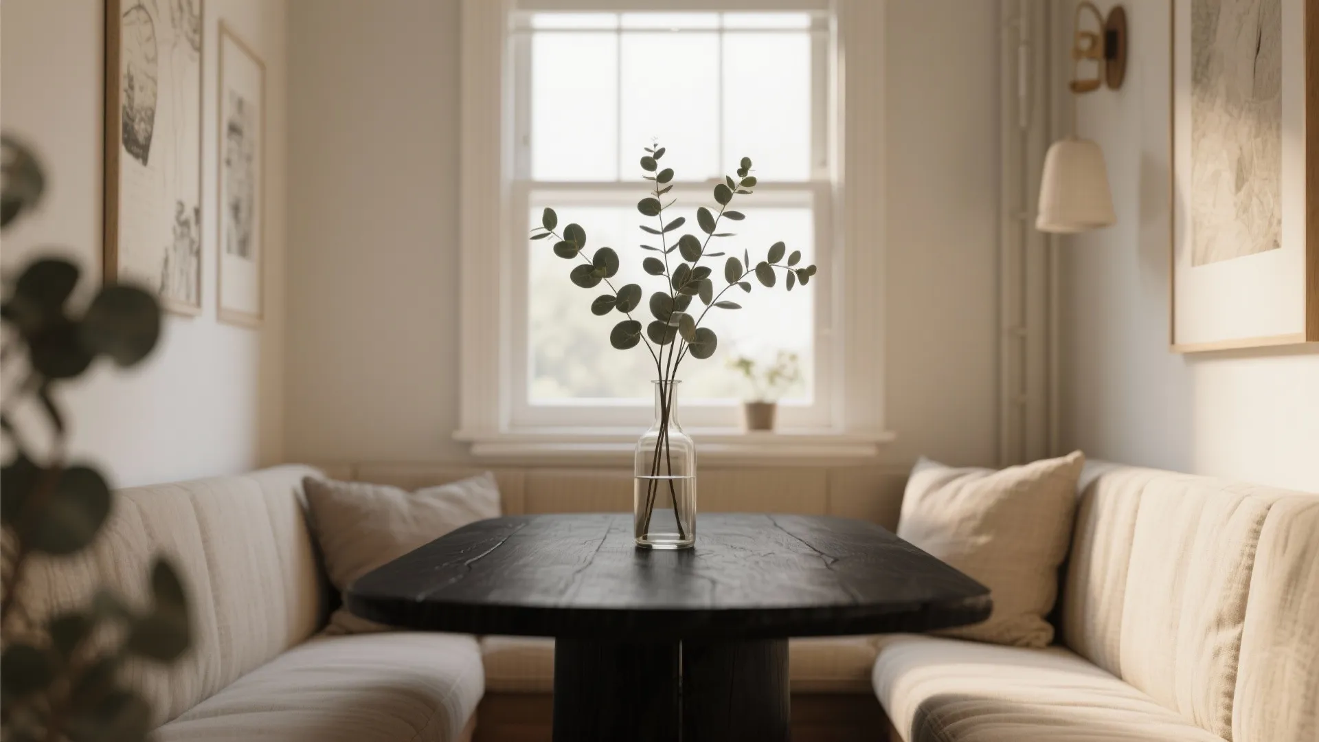 Modern breakfast nook with black wooden table and glass vase featuring green leaves near window