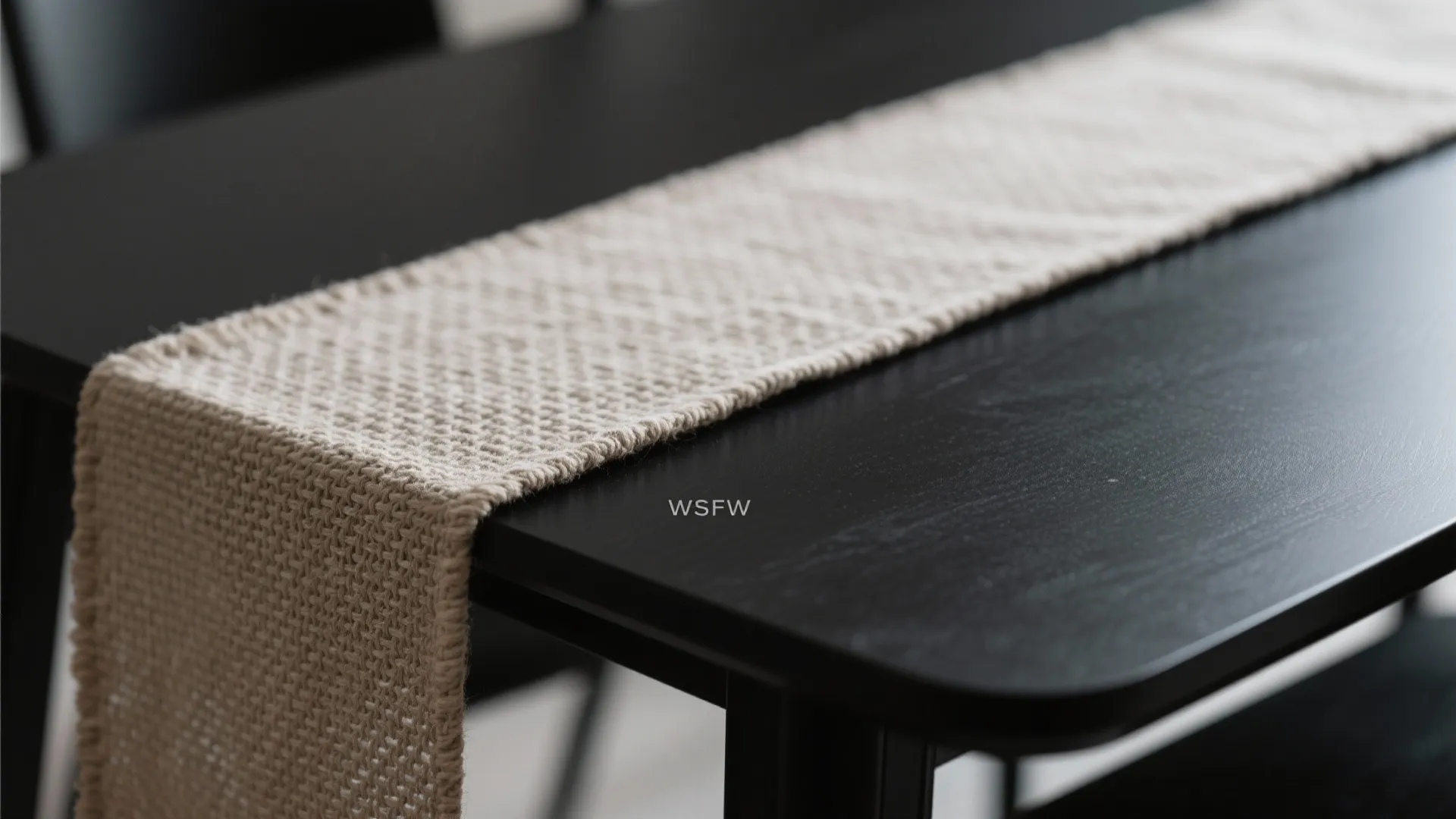 Close up of a woven beige fabric runner placed on a smooth black wooden table